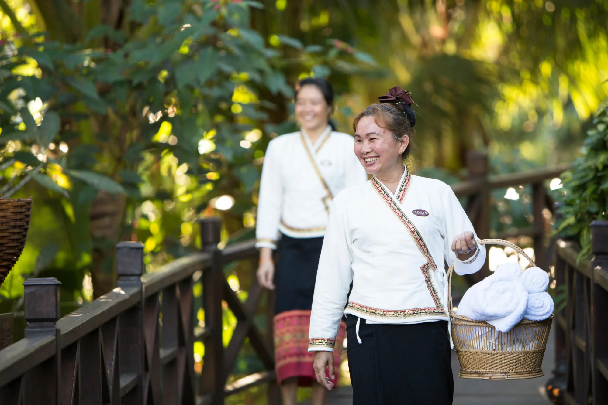 Staff members in traditional dress smiling as they walk through the gardens with a basket of towels