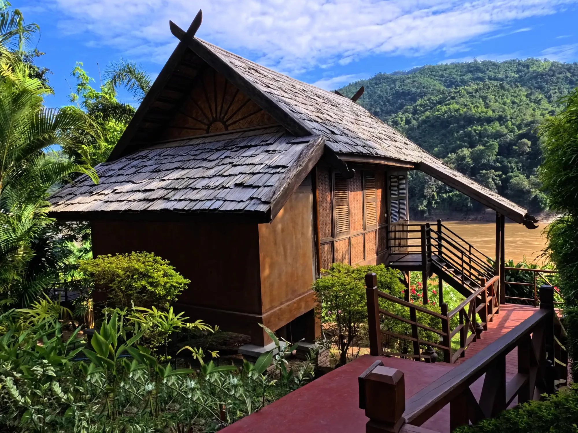 Bungalow with a peaked shingle roof and wooden railing overlooking the Mekong River
