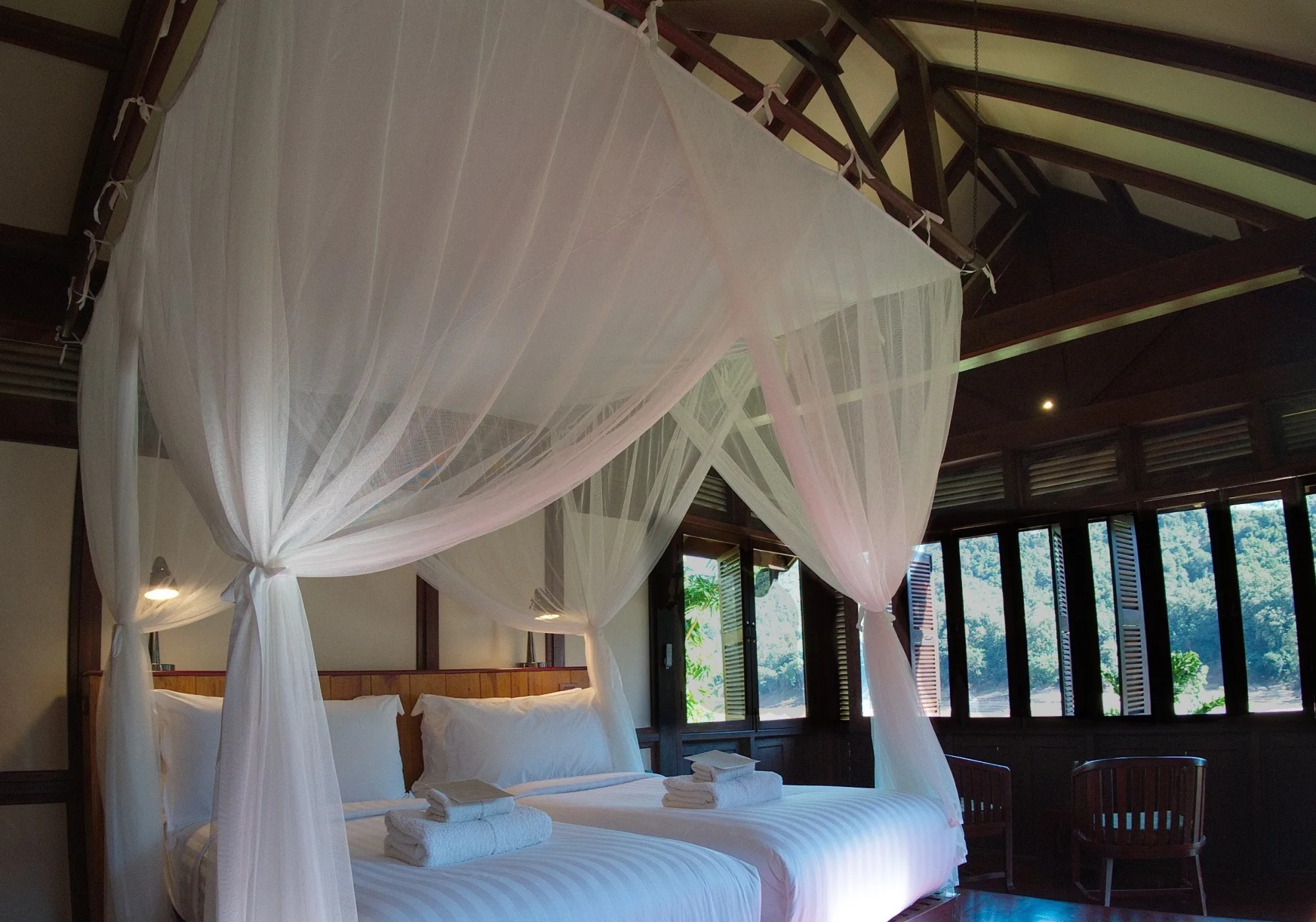 Twin beds under a shared mosquito net with the river visible through the windows