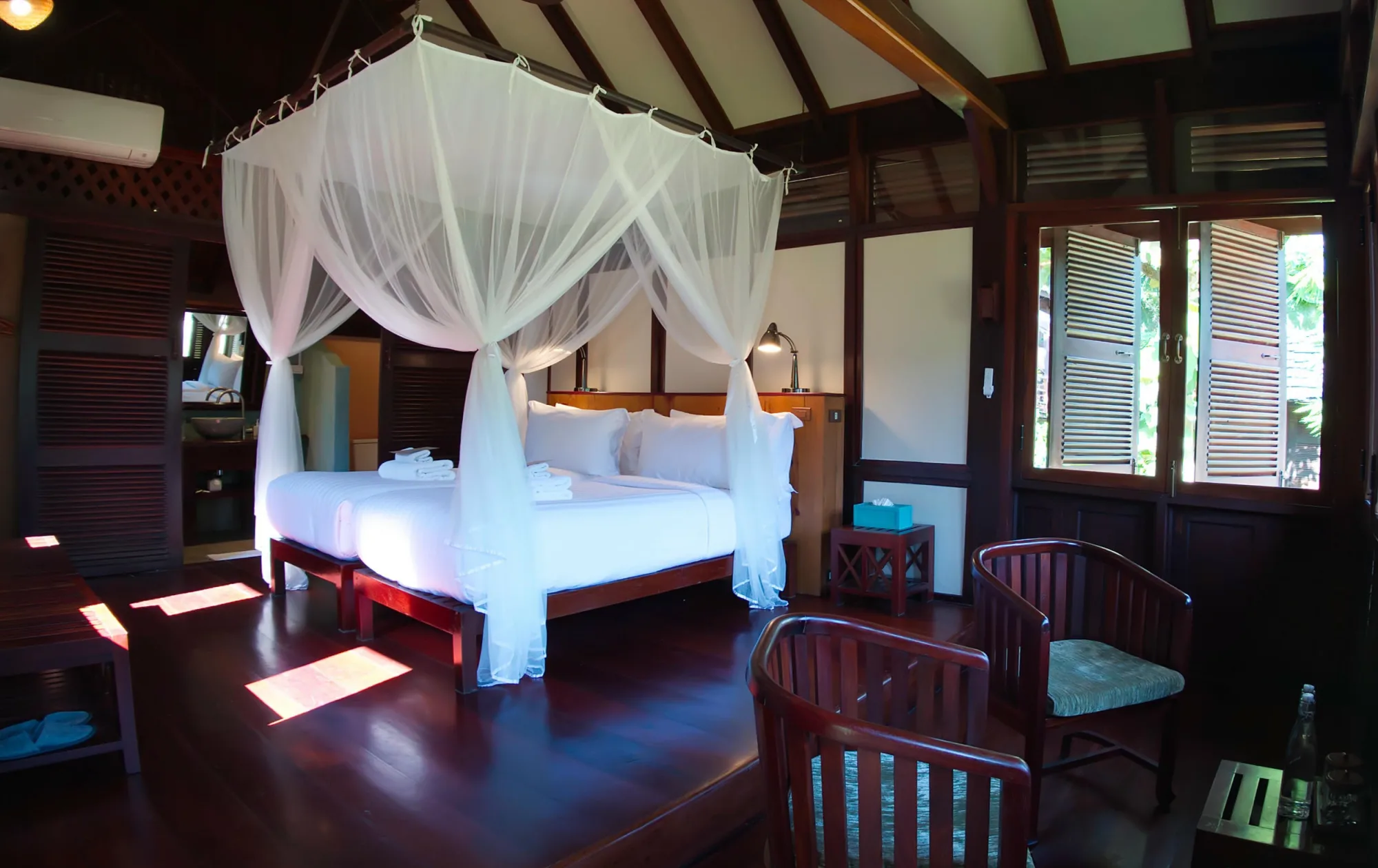 Twin-bed bungalow with a mosquito net, wooden armchairs and open shutters
